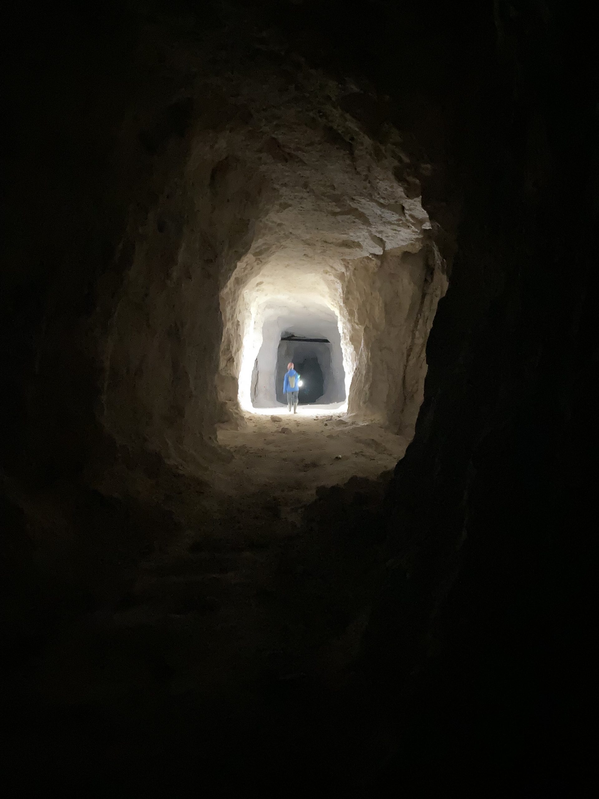 Une vue en contre-plongée d'un puits de lumière dans un tunnel souterrain, éclairant faiblement les parois rugueuses et offrant un aperçu d'une personne.